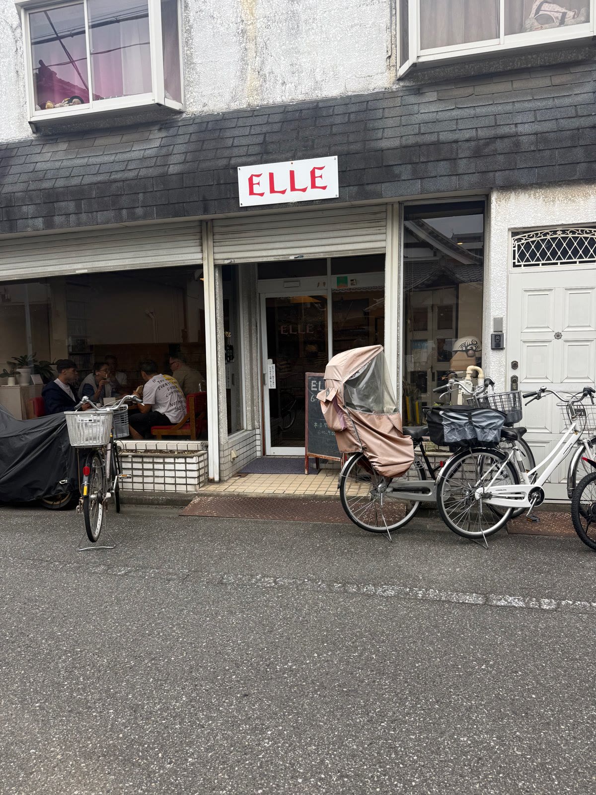 自転車が並ぶ通りに面した、白い看板を掲げた喫茶店の外観