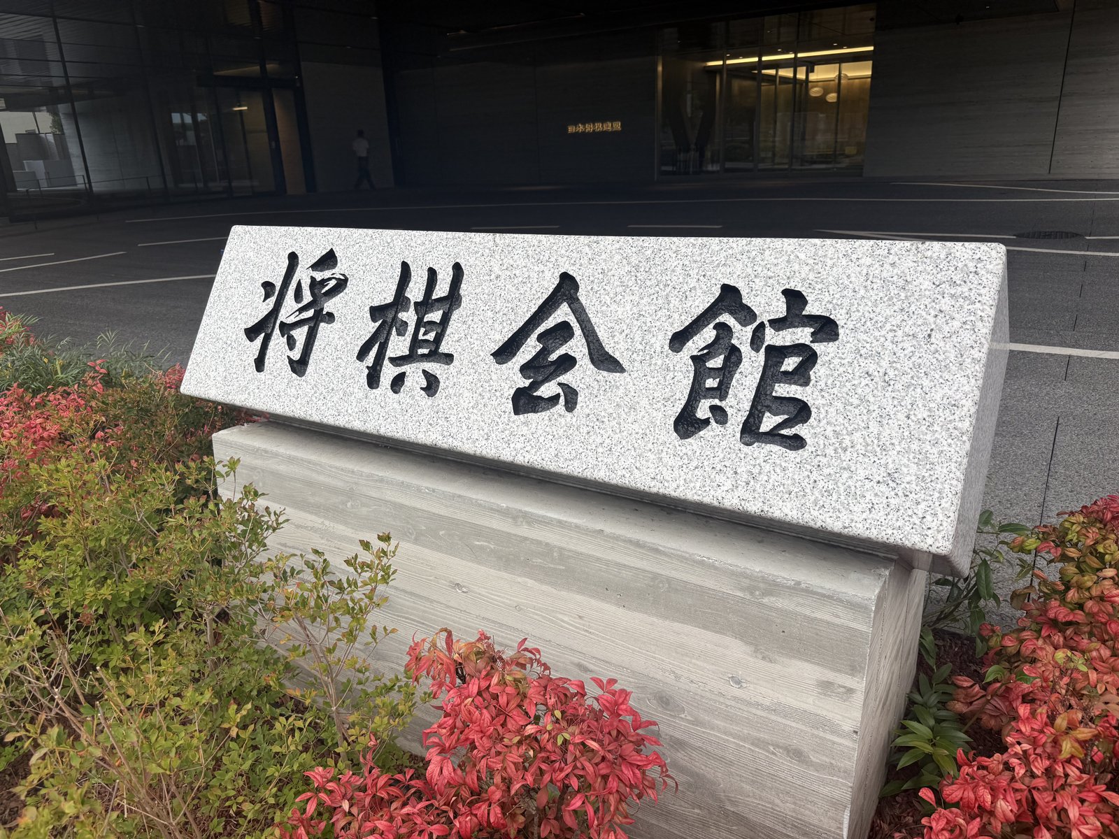 「将棋会館」と彫られた石碑と、建物前の赤い植え込み